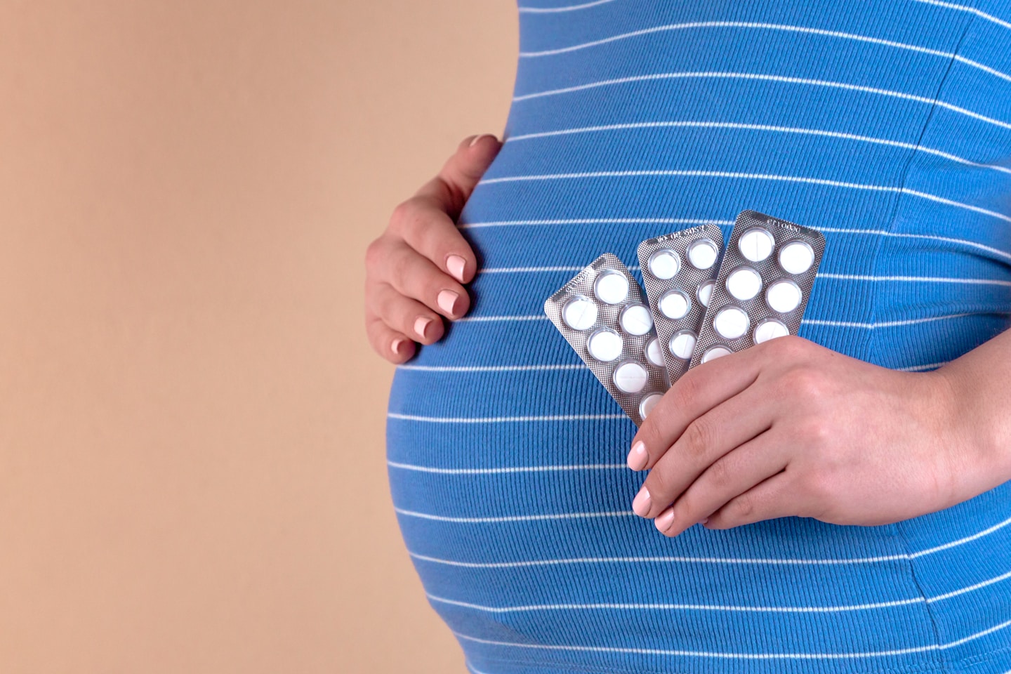 A close-up view of the belly of a pregnant woman in a blue T-shirt, which holds pills in her hands. The concept of medicine during pregnancy